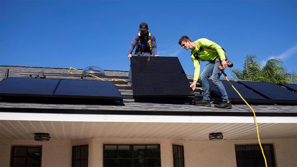 Two roofing contractors performing solar panel removal before roof replacement